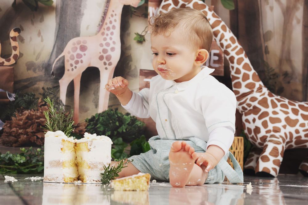 A small child in white sits among plush giraffe toys and decorative elements during a photo session.