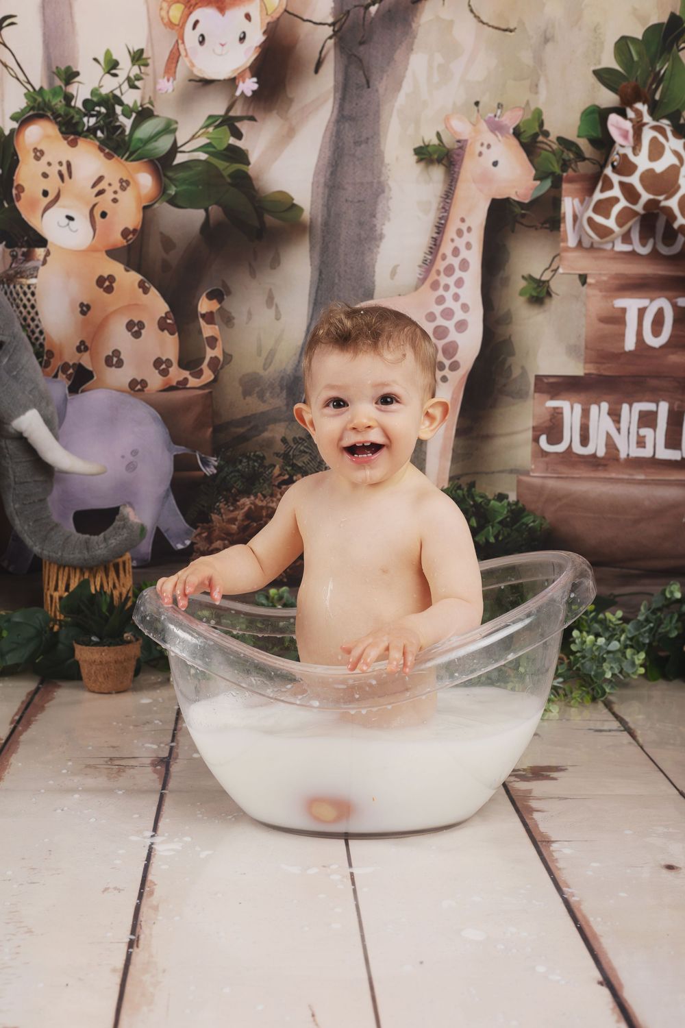 A joyful bath time scene with safari-themed decorations and a clear plastic tub on wooden flooring.
