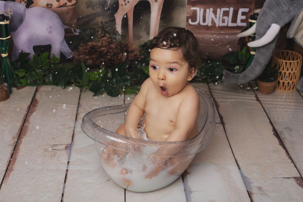 A baby sits in a vintage-style metal wash basin filled with soapy water during bath time.
