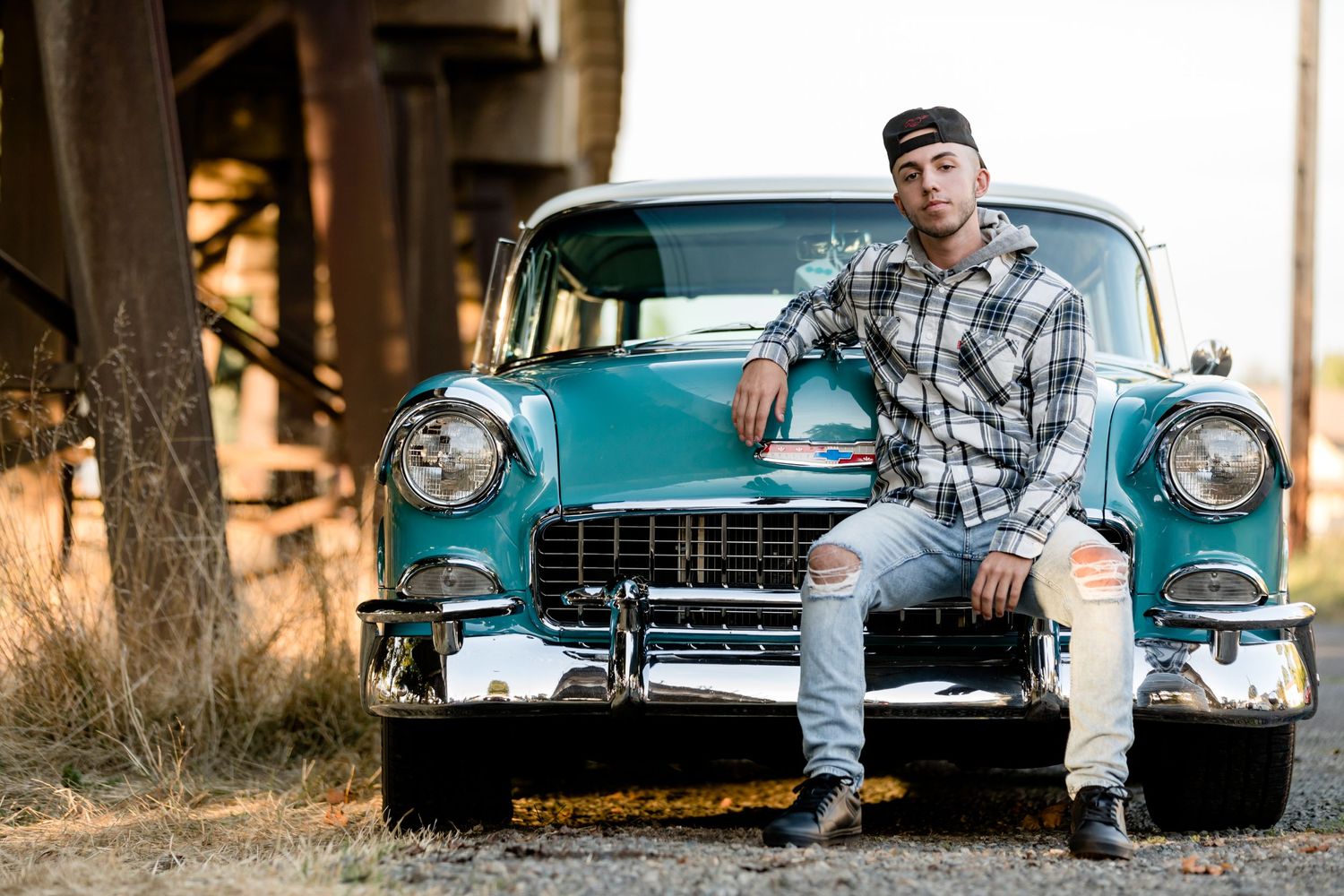 A classic turquoise Chevrolet from the 1950s parked in a rustic outdoor setting with fall foliage.