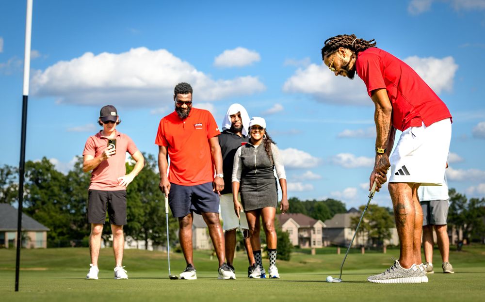 Group of people on a golf course enjoying a sunny day as someone attempts a putt on the green.