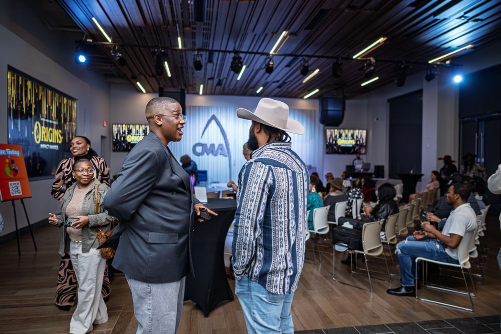 People gather at a networking event in a modern venue with blue lighting and CMA branding on the wall.