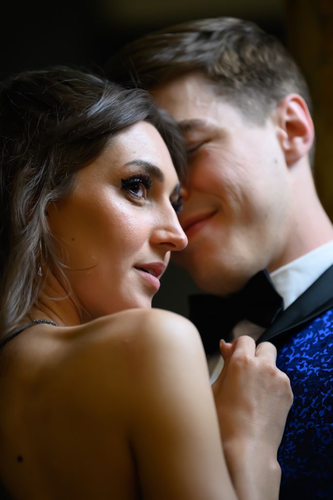 Elegant couple in formal attire share an intimate moment, woman in backless dress, man in blue tuxedo jacket.