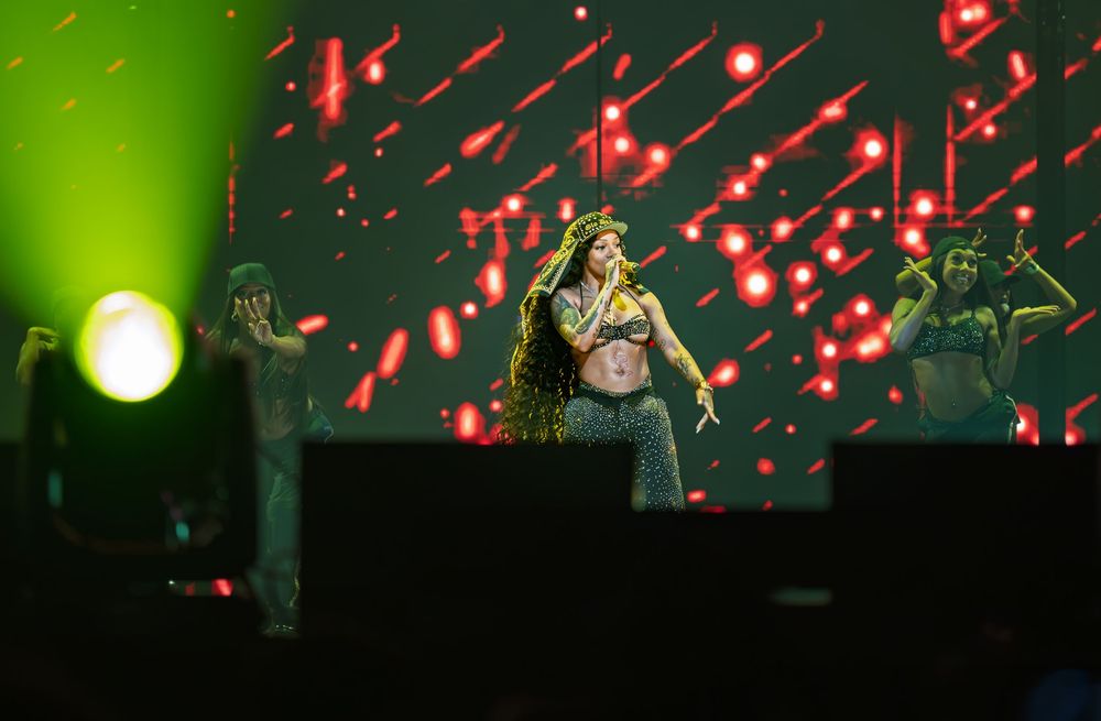 Concert performer silhouetted on stage with red lighting effects and confetti falling in the background.