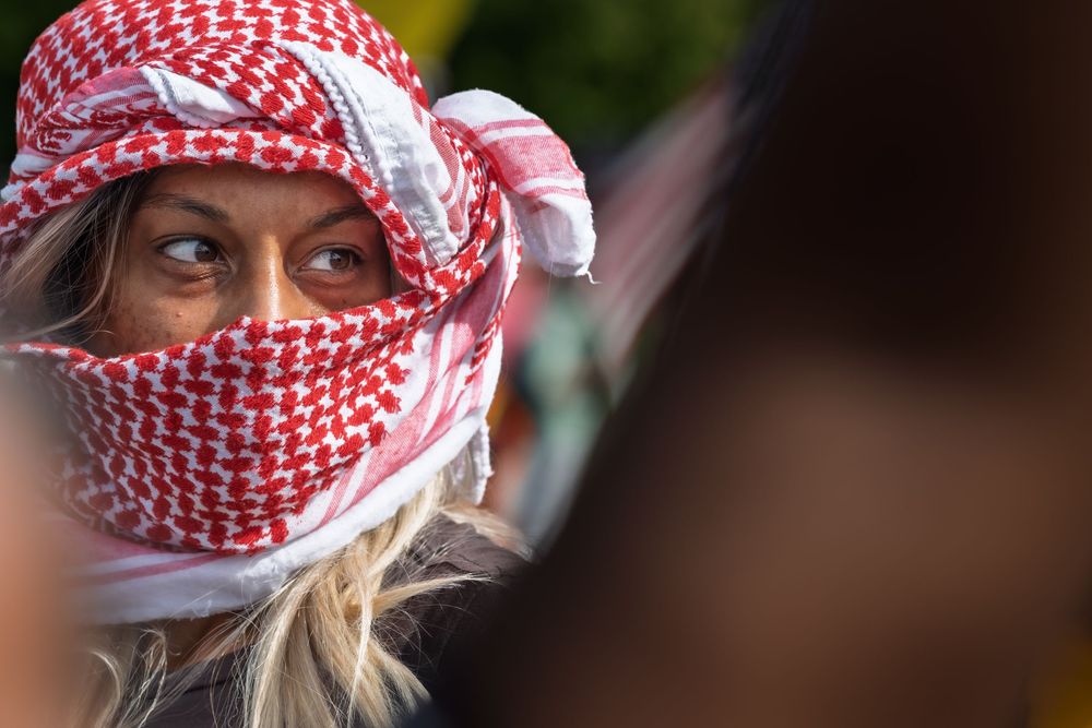 Person wearing traditional red and white keffiyeh headscarf looks to the side in close-up portrait.
