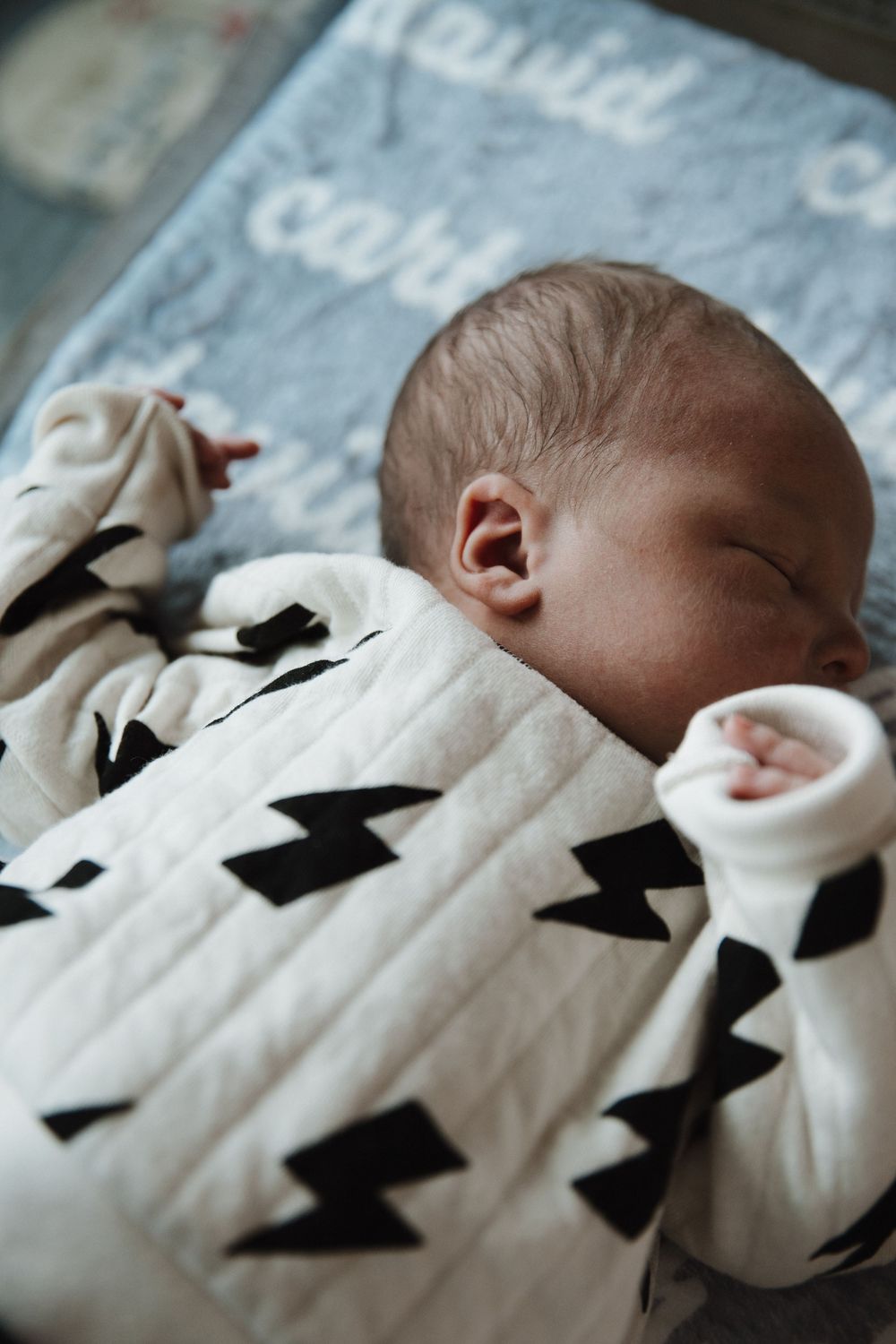 Sleeping baby wearing white pajamas with black lightning bolt pattern on soft blue blanket.