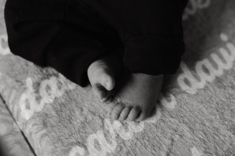 Black and white close-up photograph of a small bare foot on textured carpet.