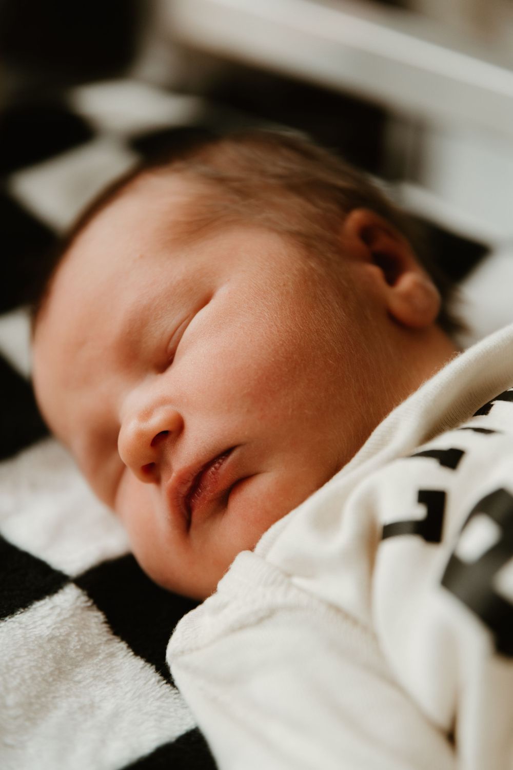Peaceful sleeping newborn baby on black and white checkered blanket.