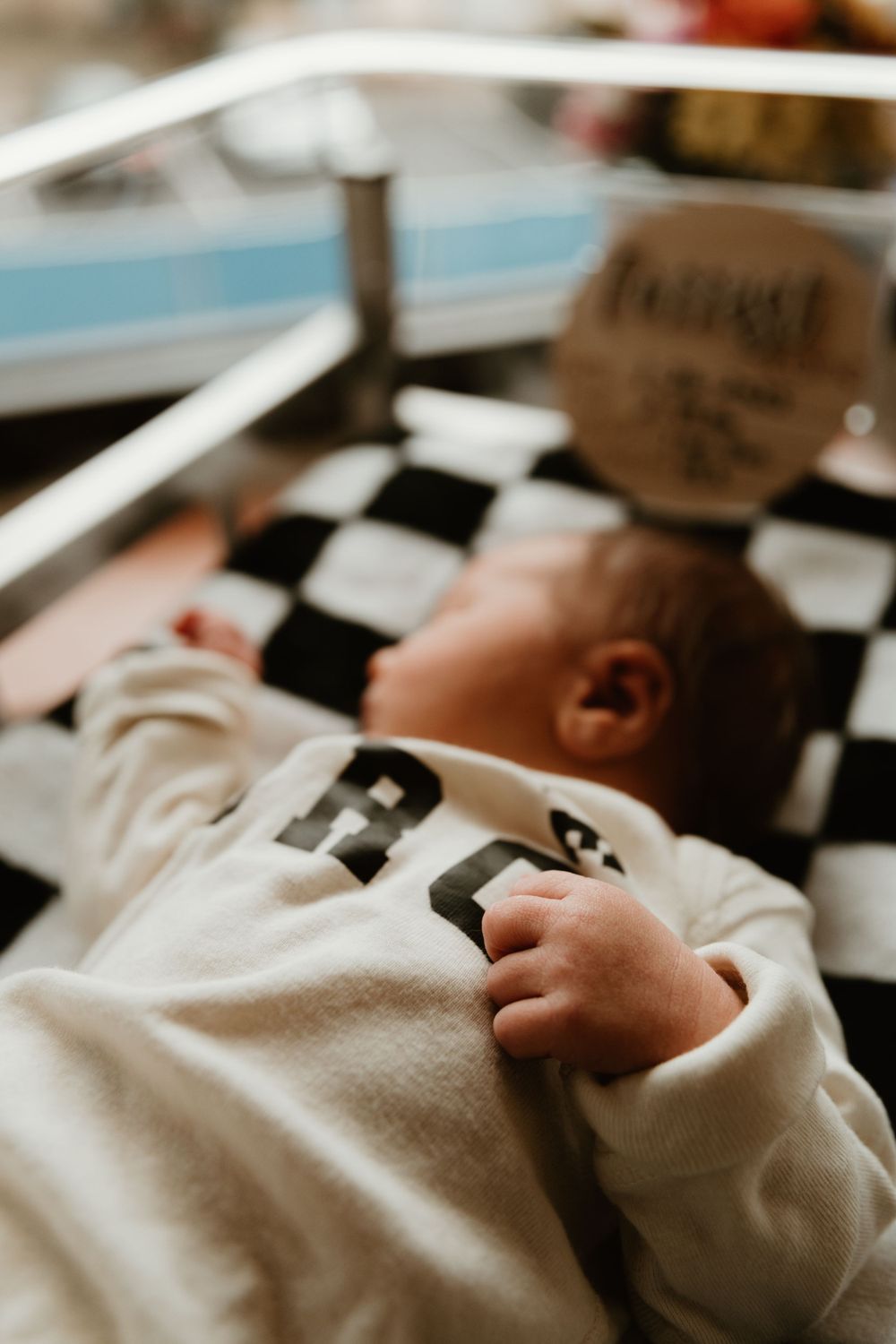 Close-up of a sleeping infant's hands and white clothing in soft natural light.