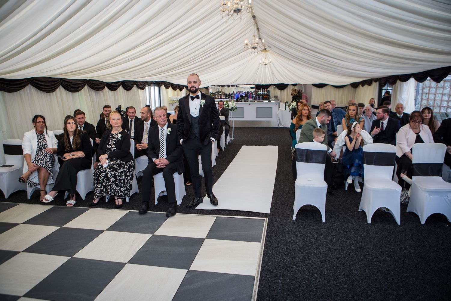 Wedding reception venue with black and white checkered dance floor and white draped ceiling.