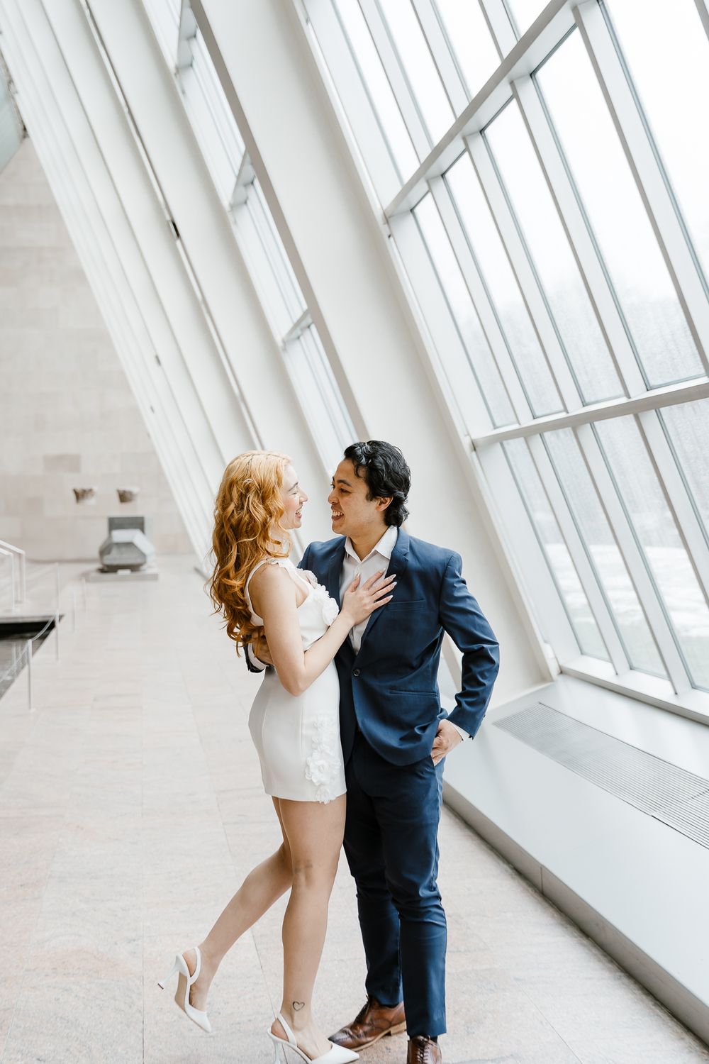 A romantic moment shared between two people in formal attire against a bright modern interior with slanted windows.