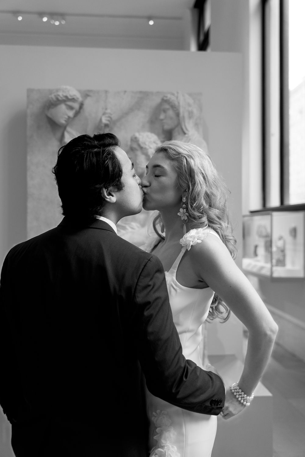 A romantic black and white photograph of a couple sharing an intimate kiss in what appears to be an art gallery.
