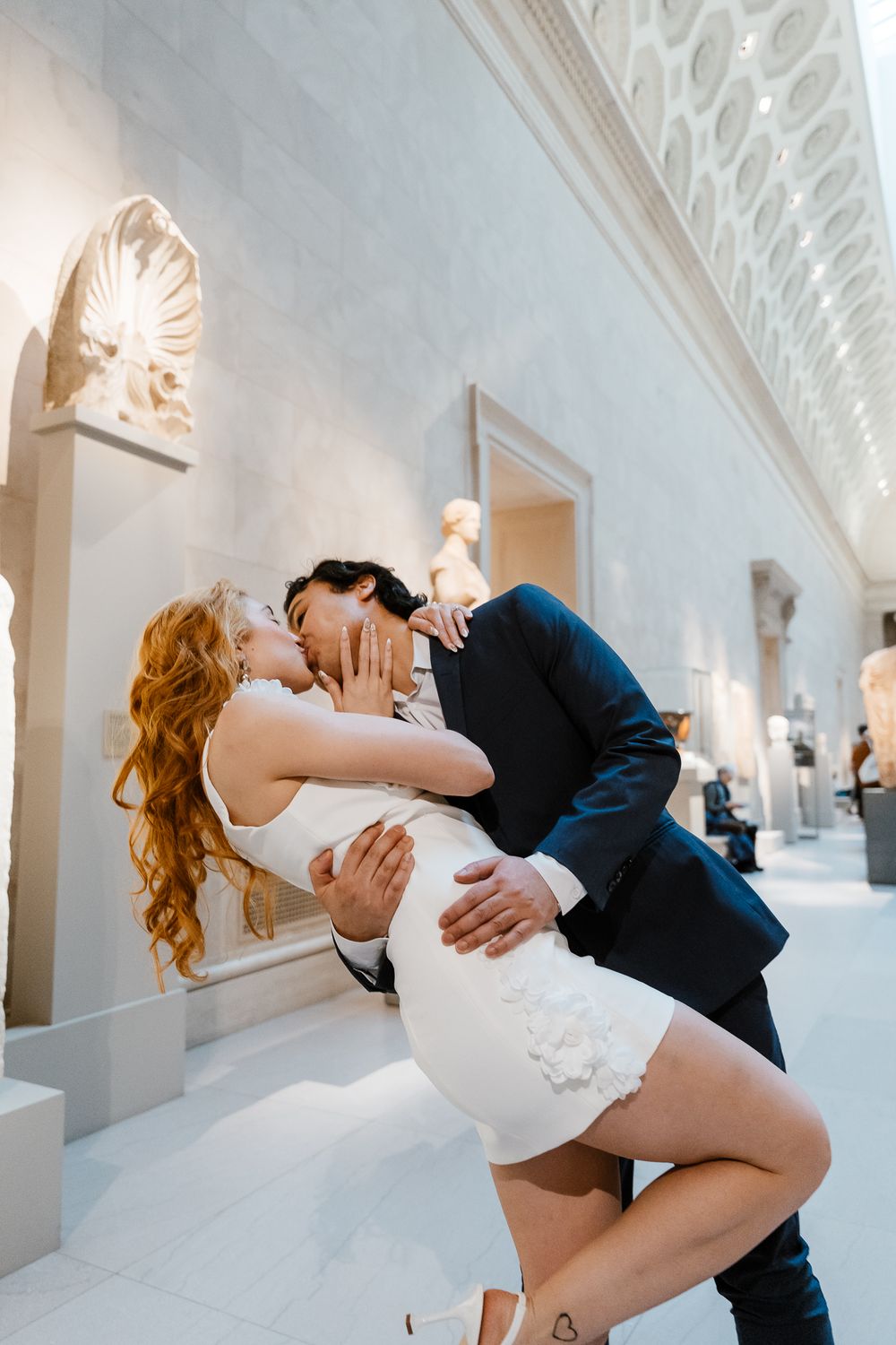 A romantic dip kiss in an elegant white hallway with ornate architectural details and decorative wall sconces.