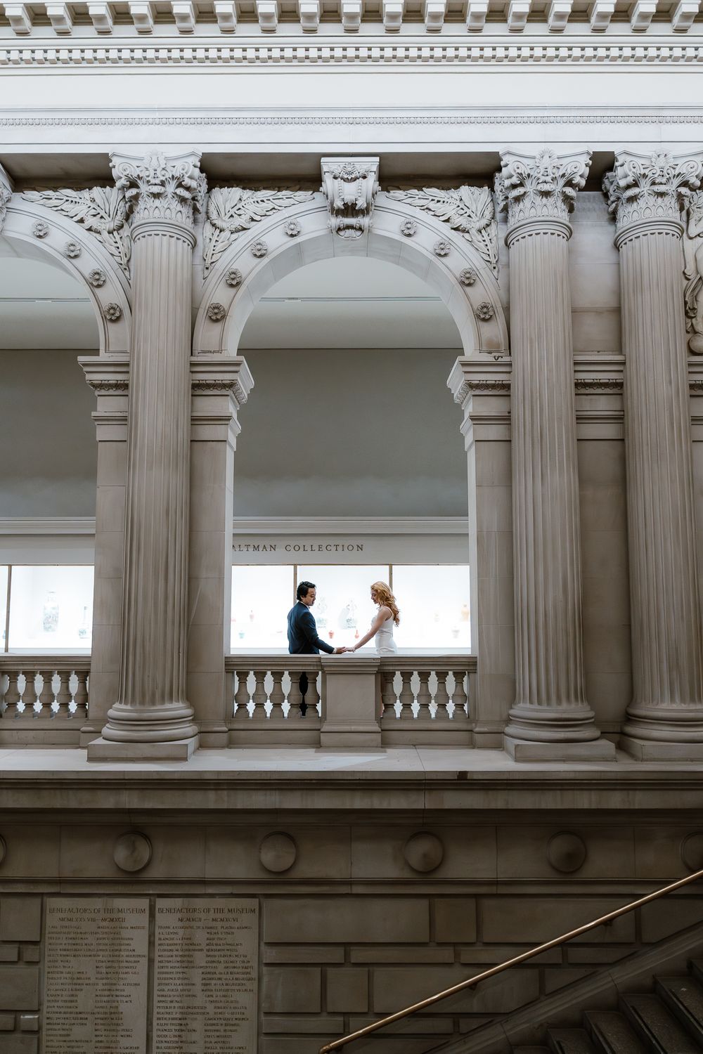 Ornate classical architecture with Corinthian columns frames two figures silhouetted against a bright window in a grand interior.