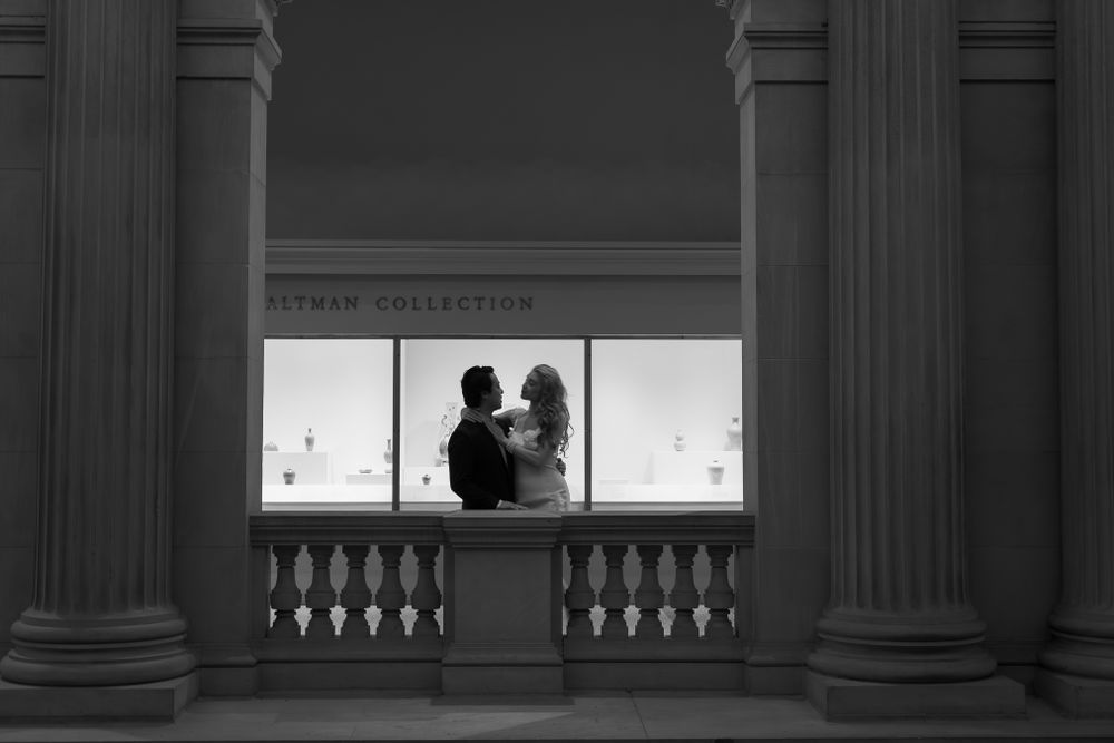 Silhouette of couple framed by classical columns against bright window display in museum or gallery.