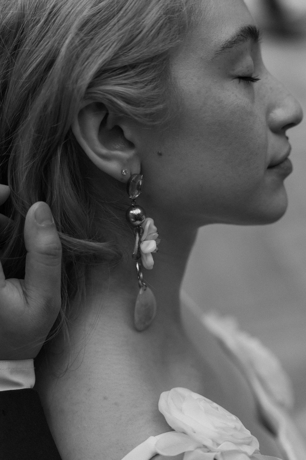 Close-up black and white profile shot showing delicate floral drop earrings and soft natural lighting.