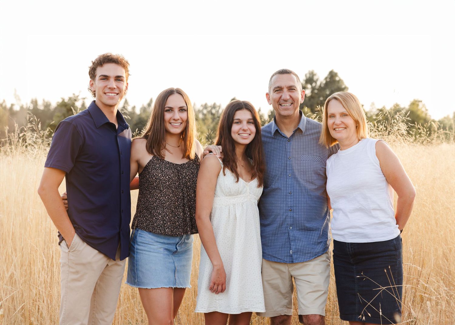 A group of five people pose together outdoors in a golden wheat field on a sunny day.