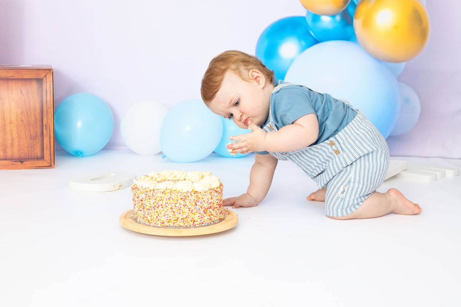 Cake smash photo session setup with blue and gold balloons and a decorated cake for a first birthday celebration.