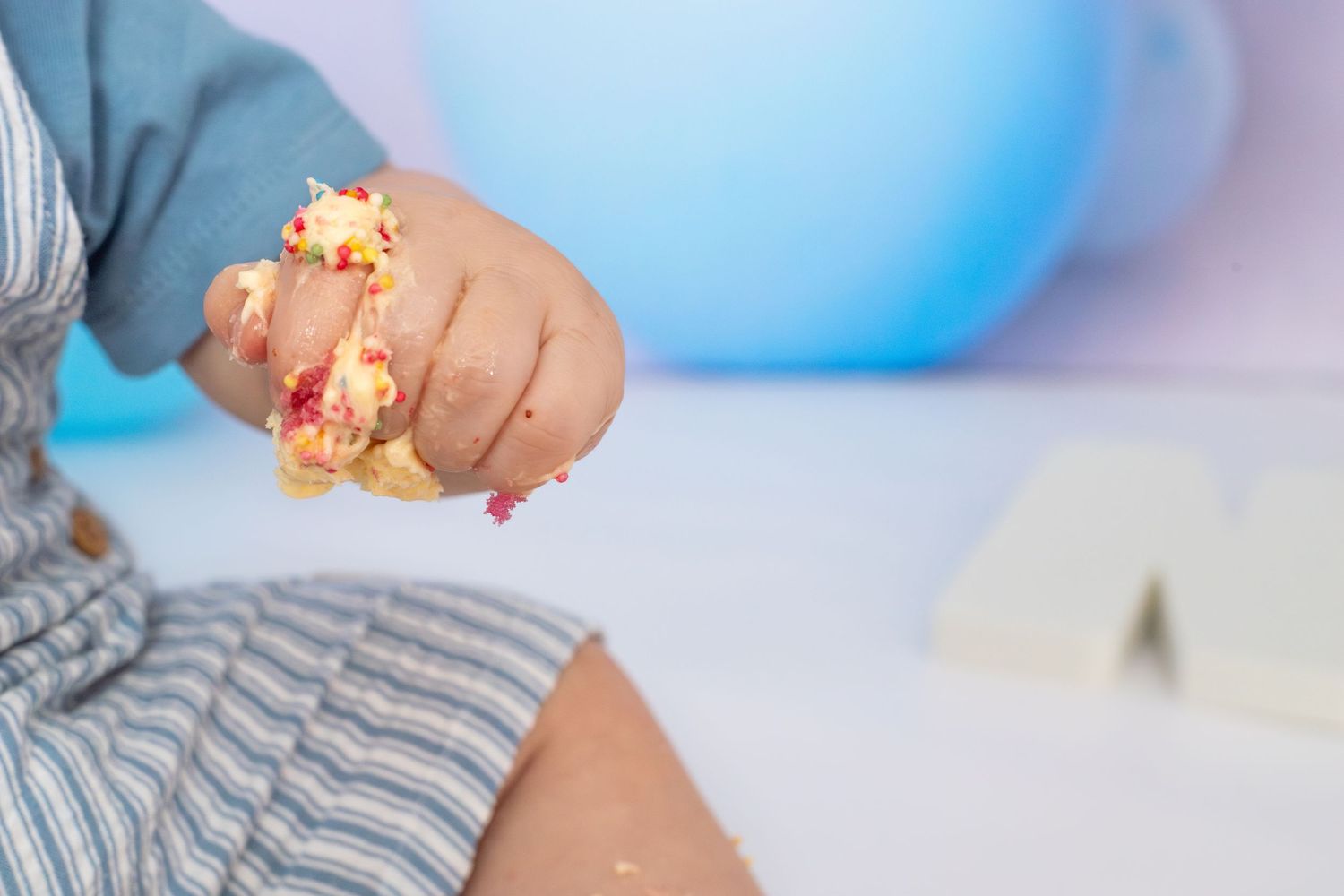 Close-up of small hands reaching for birthday cake during cake smash photo session.