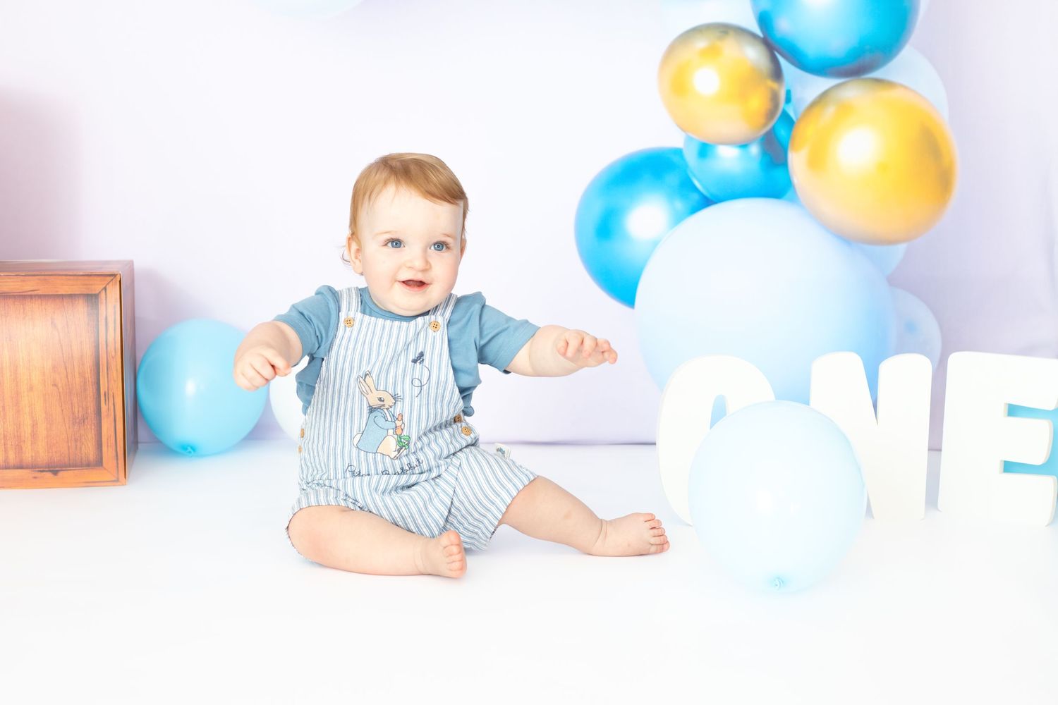 First birthday photo setup with blue and yellow balloons against white backdrop.