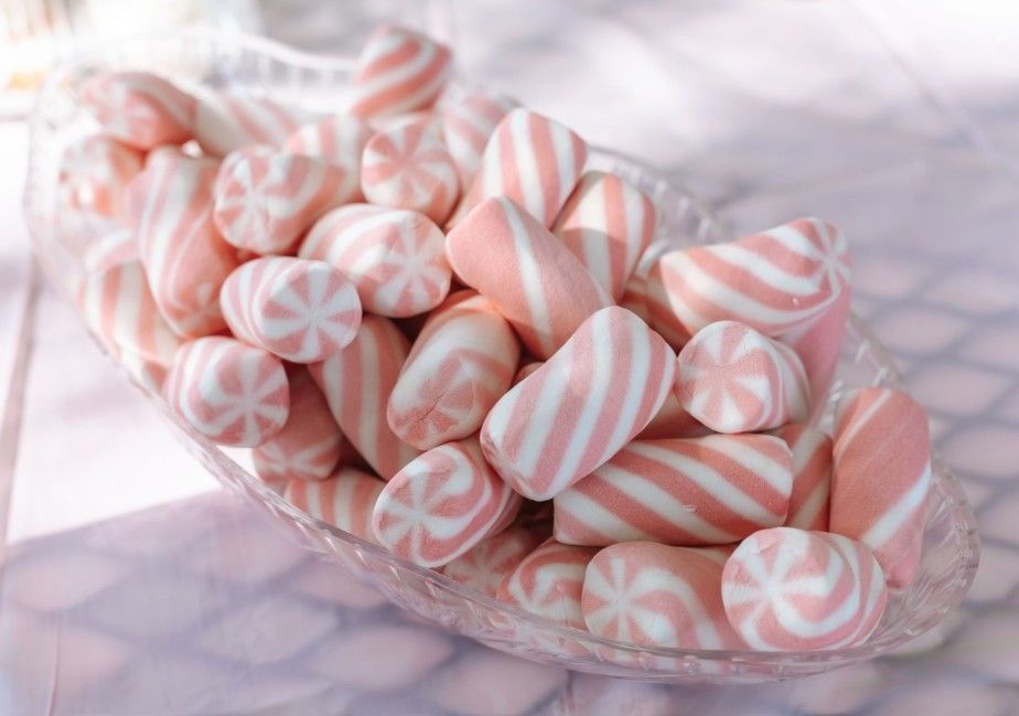 Pink and white striped butter mints arranged in a glass bowl on a soft white surface.