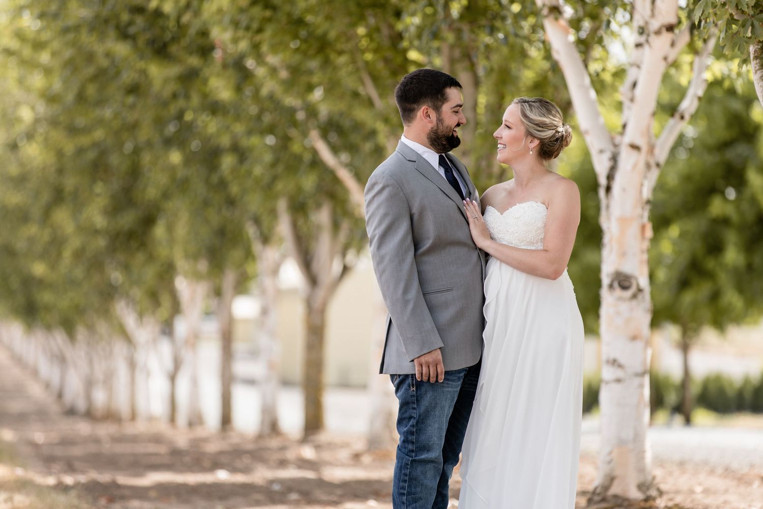 Couple sharing an intimate moment among a row of birch trees in their wedding attire.