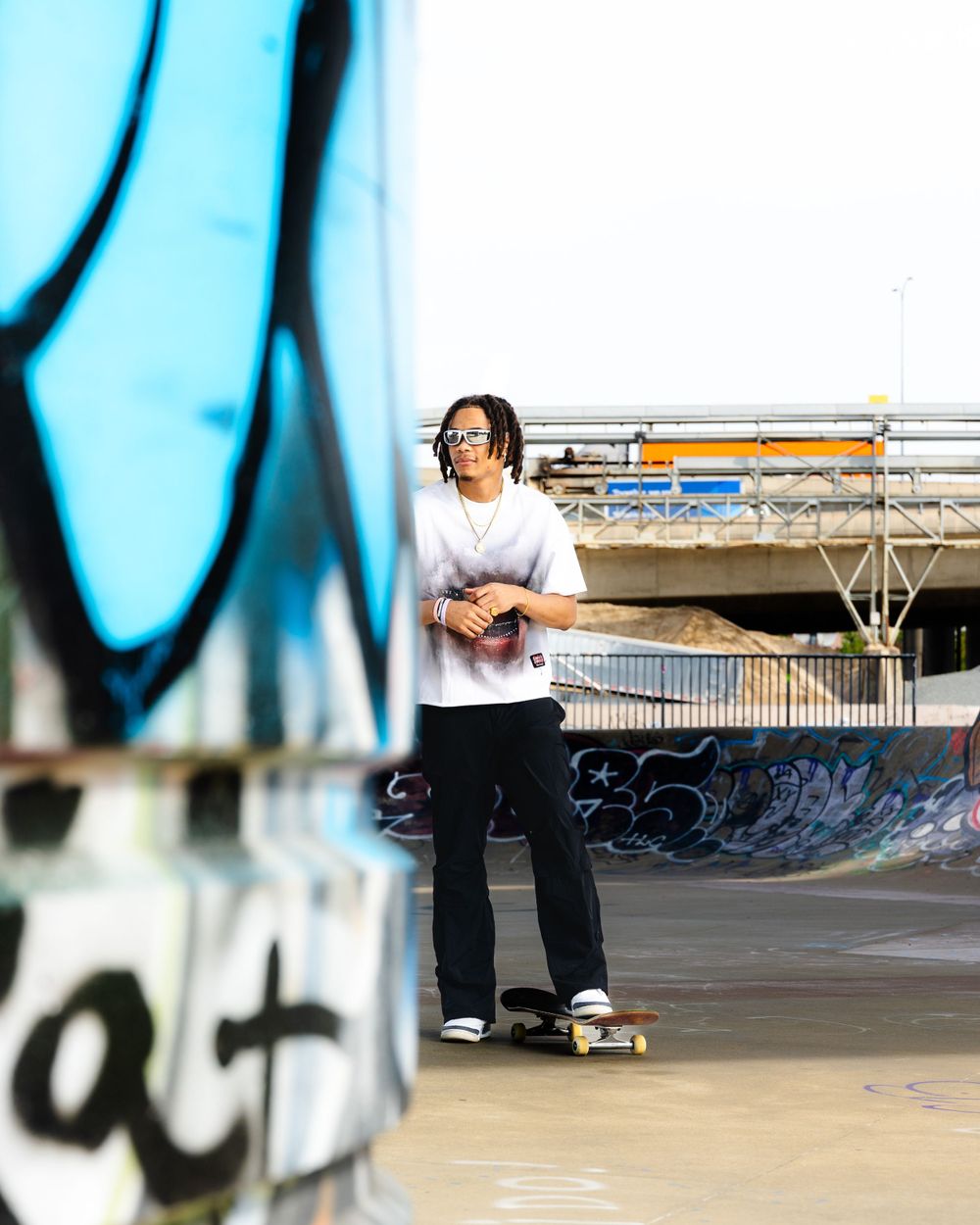 Skateboarder practicing tricks at a graffiti-covered skate park with a blue-tinted urban backdrop.