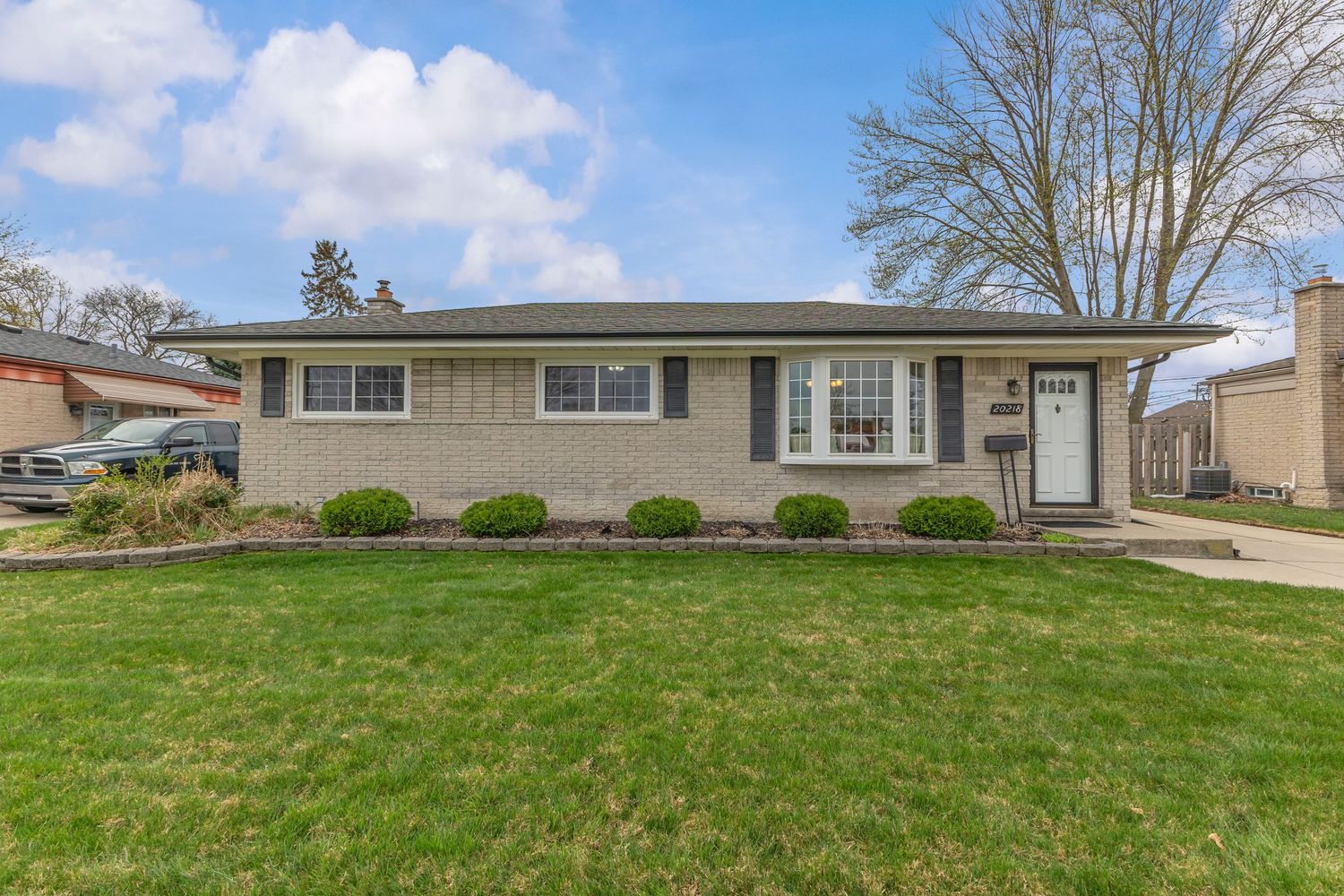 Charming white clapboard bungalow with covered front porch, brick garage, and small front yard.