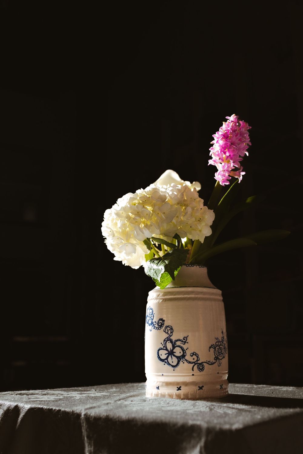 White hydrangea and pink hyacinth flowers in a vintage ceramic vase with blue floral design on a dark background.