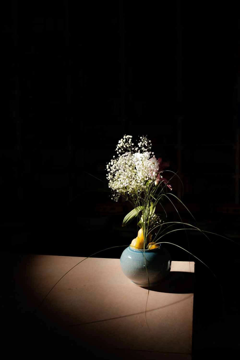 Blue ceramic vase with white baby's breath flowers spotlit on a dark table.