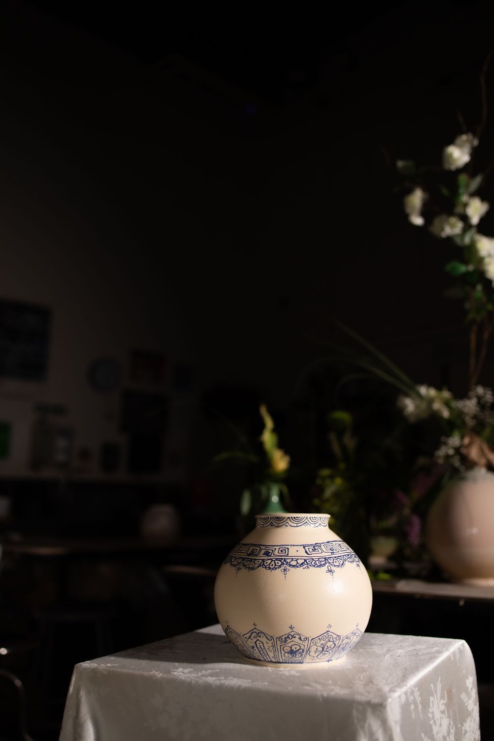 Vintage ceramic vase with blue floral motifs on white glaze, displayed on a table in a dimly lit room.