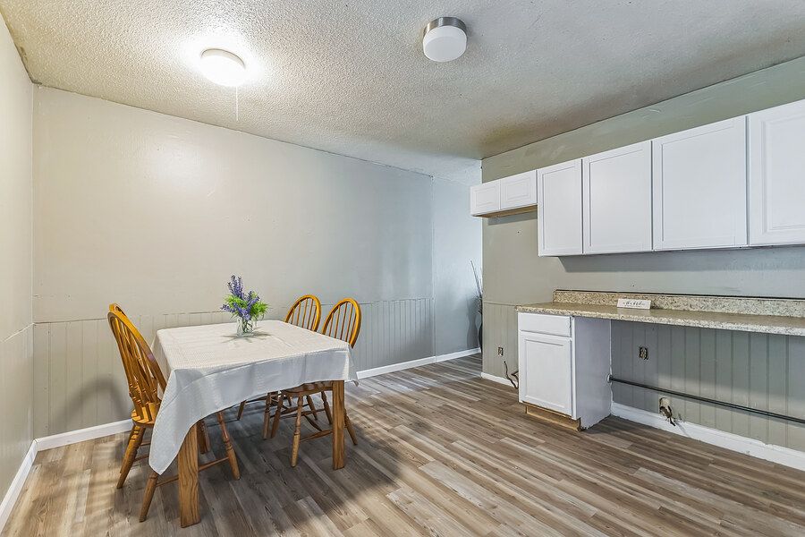 Bright dining area with white cabinets, wood-look floors, small table with chairs, and a vase of purple flowers.