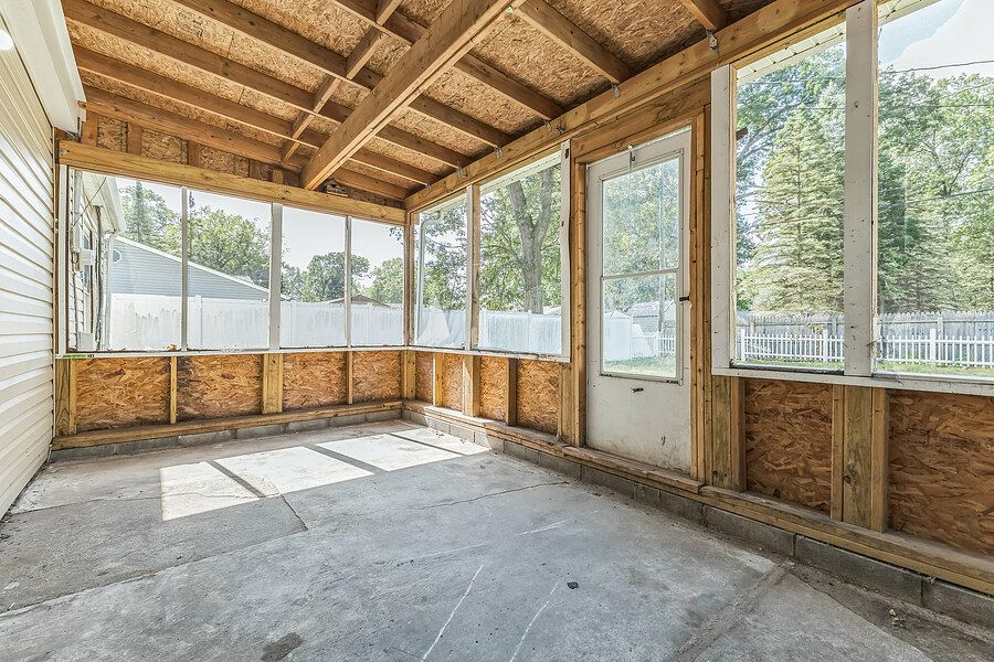 Unfinished screened porch with wood-framed walls, concrete floor, and large windows overlooking a fenced backyard.