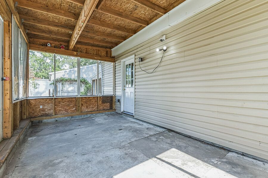 Covered concrete patio with wood beam ceiling, vinyl siding, and a white door leading into the home.