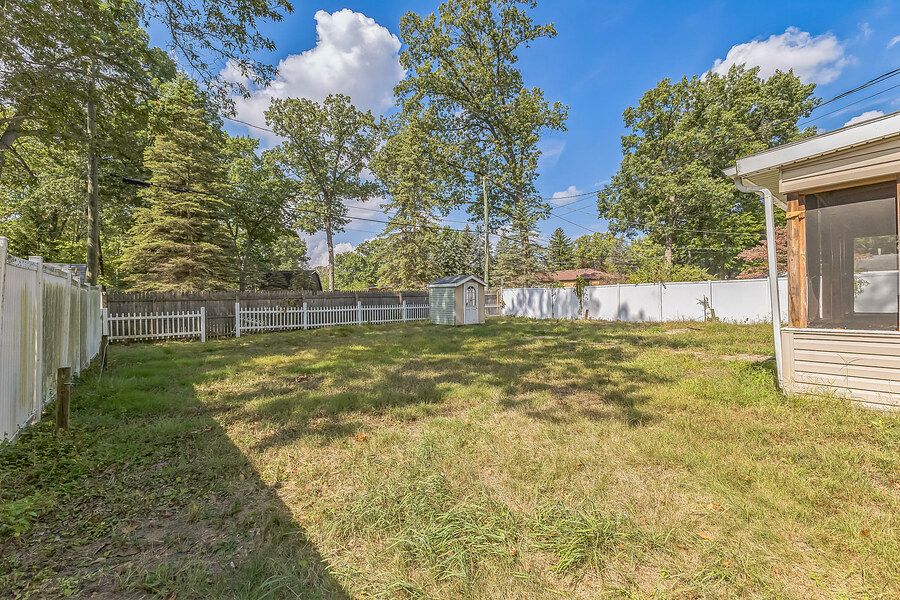 Spacious backyard with lush green grass, mature trees, and white vinyl privacy fence on a sunny day.