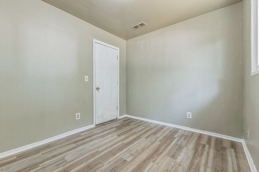 Empty bedroom with light gray walls, luxury vinyl plank flooring, white door, and visible air vent.