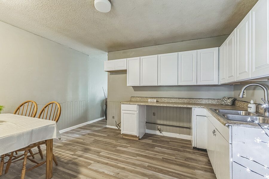 Kitchen with white cabinets, wood-look flooring, and sink near dining area.