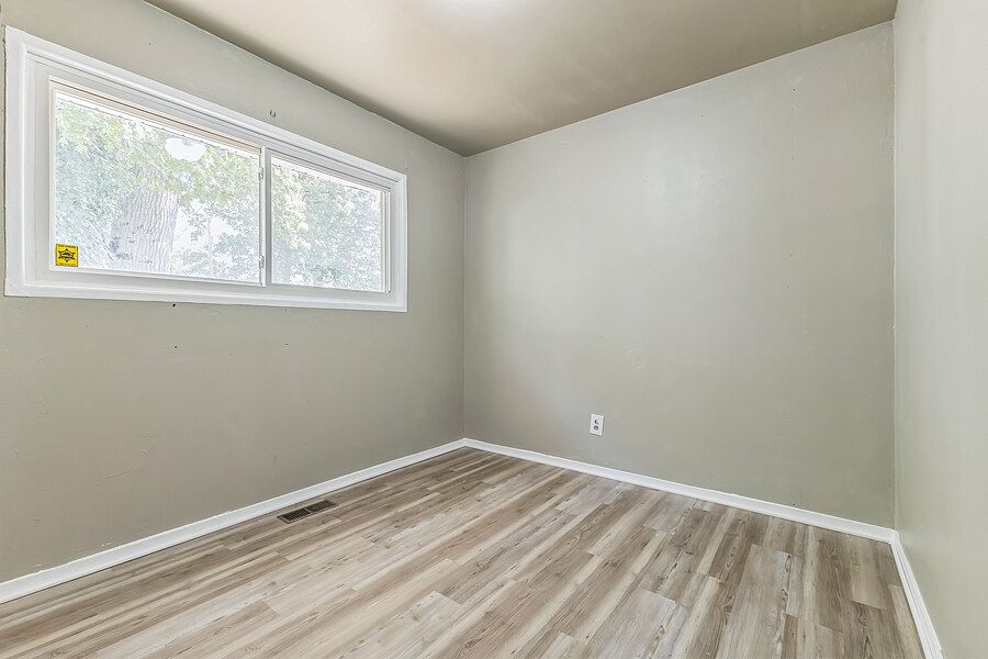 Empty bedroom with light gray walls, luxury vinyl plank flooring, white baseboards, and a single window.