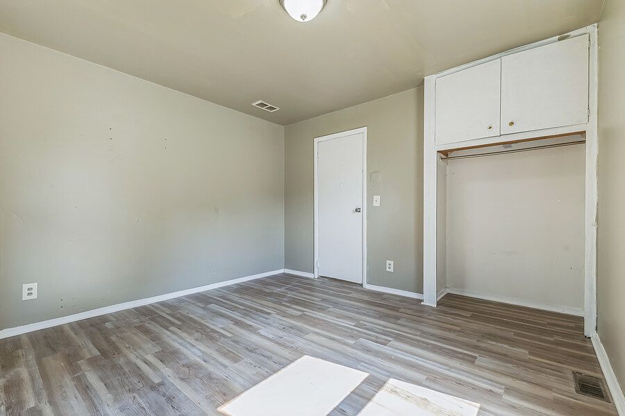 Empty bedroom with wood-look floors, white walls, closet with upper cabinet storage.