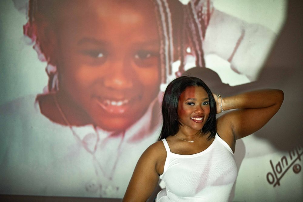 Young woman in white top smiles in front of projected childhood photo backdrop.