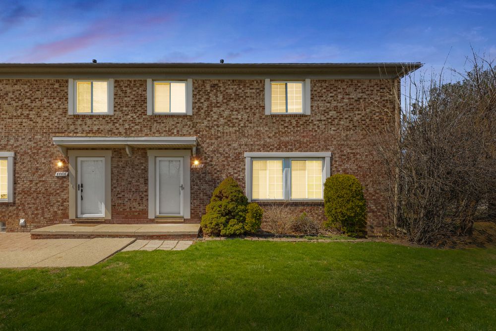 Two-story brick townhome with dual entry doors, manicured shrubs, and paved walkway at dusk.