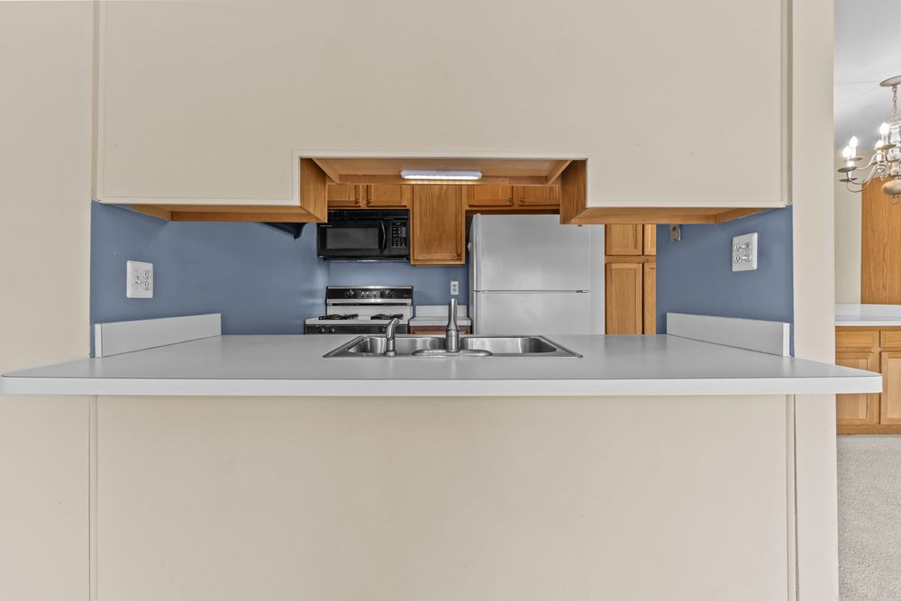 Kitchen pass-through with white countertop, oak cabinets, black appliances, and blue walls beyond.