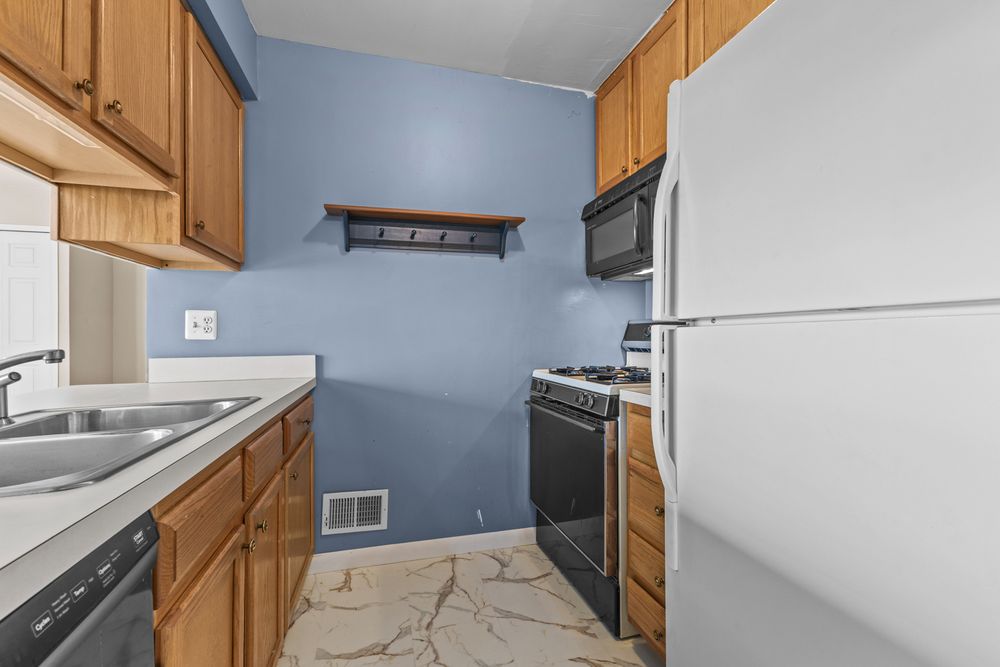 Kitchen featuring oak cabinets, black appliances, white refrigerator, blue accent wall, and tile flooring.