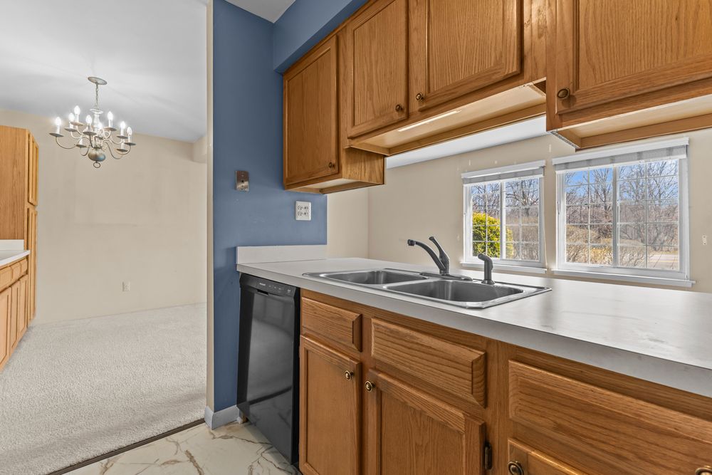 Kitchen with oak cabinets, double sink, black dishwasher, chandelier, and window overlooking outdoors.