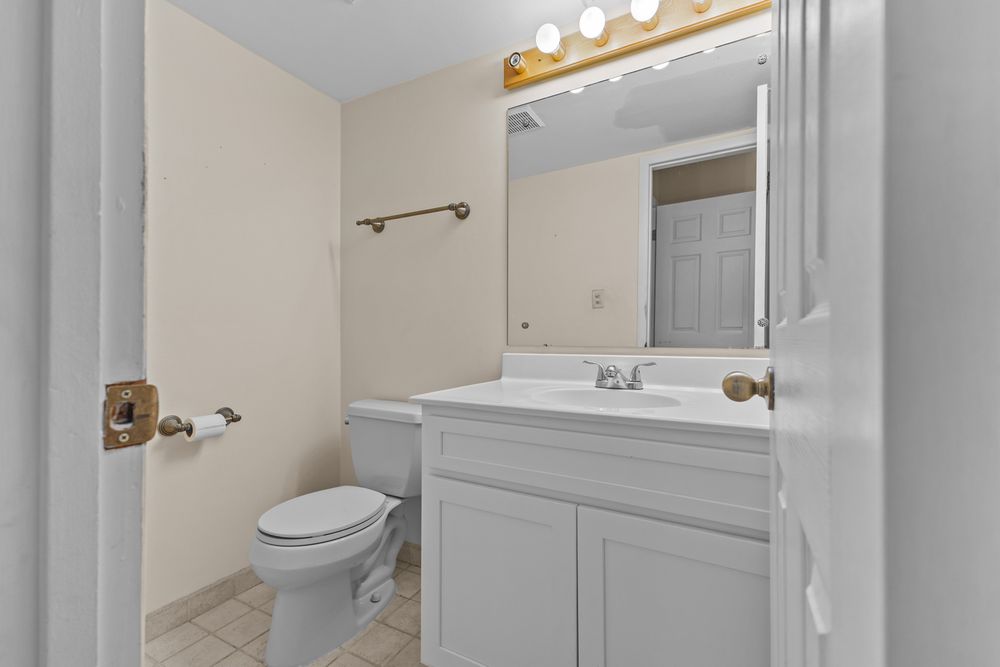 Clean bathroom with white vanity, large mirror, toilet, and tile flooring in neutral tones.