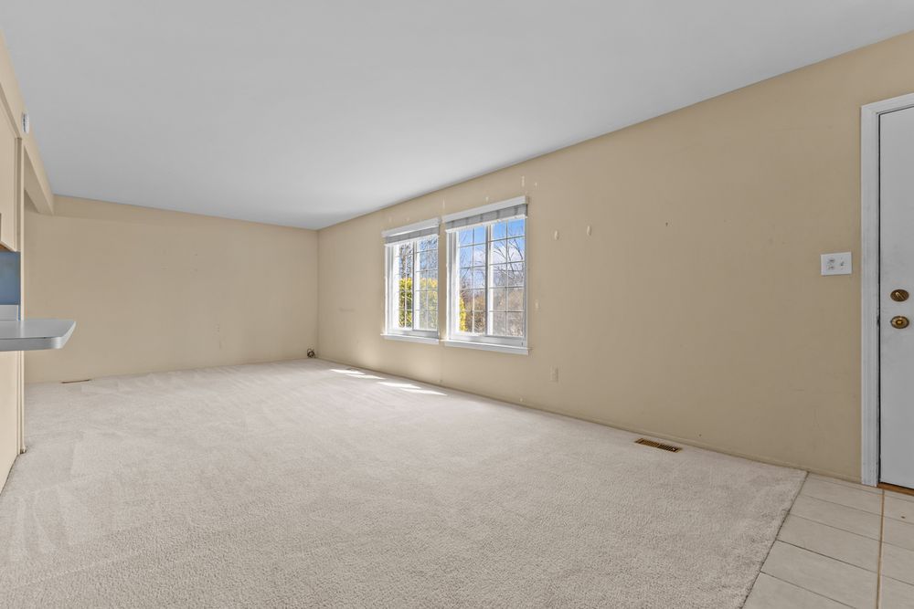 Spacious empty living room with beige carpet, neutral walls, and bright double windows.