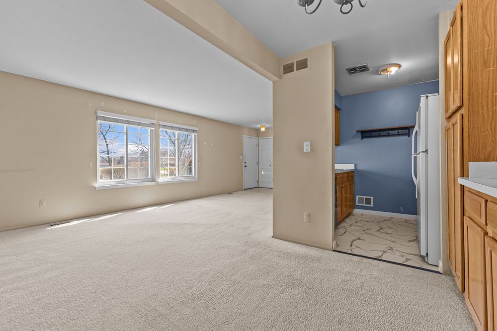 Open kitchen and living area with oak cabinets, white appliances, beige carpet, and blue accent wall.