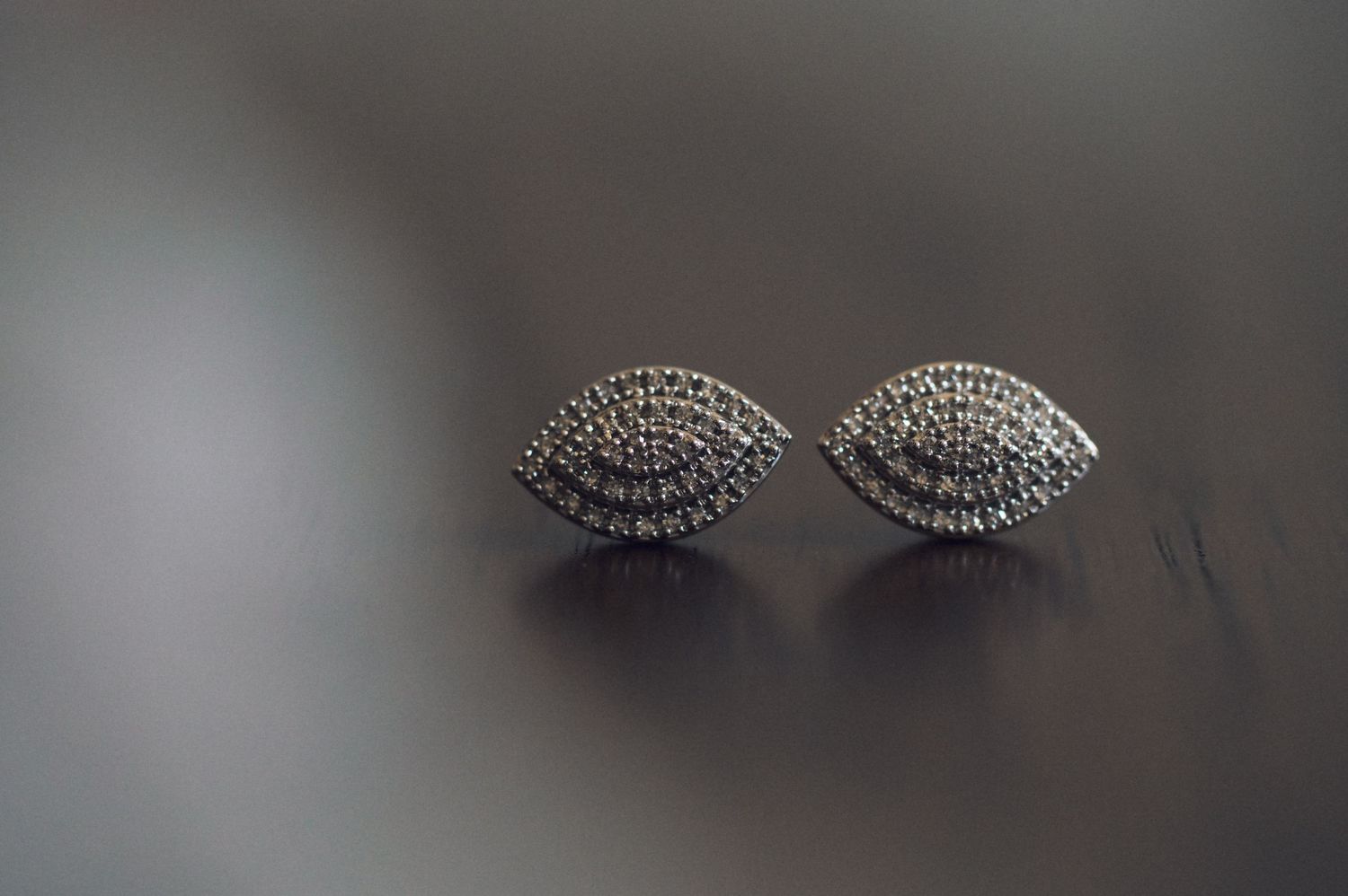 Silver marquise-shaped stud earrings with pavé diamond detailing on reflective surface.