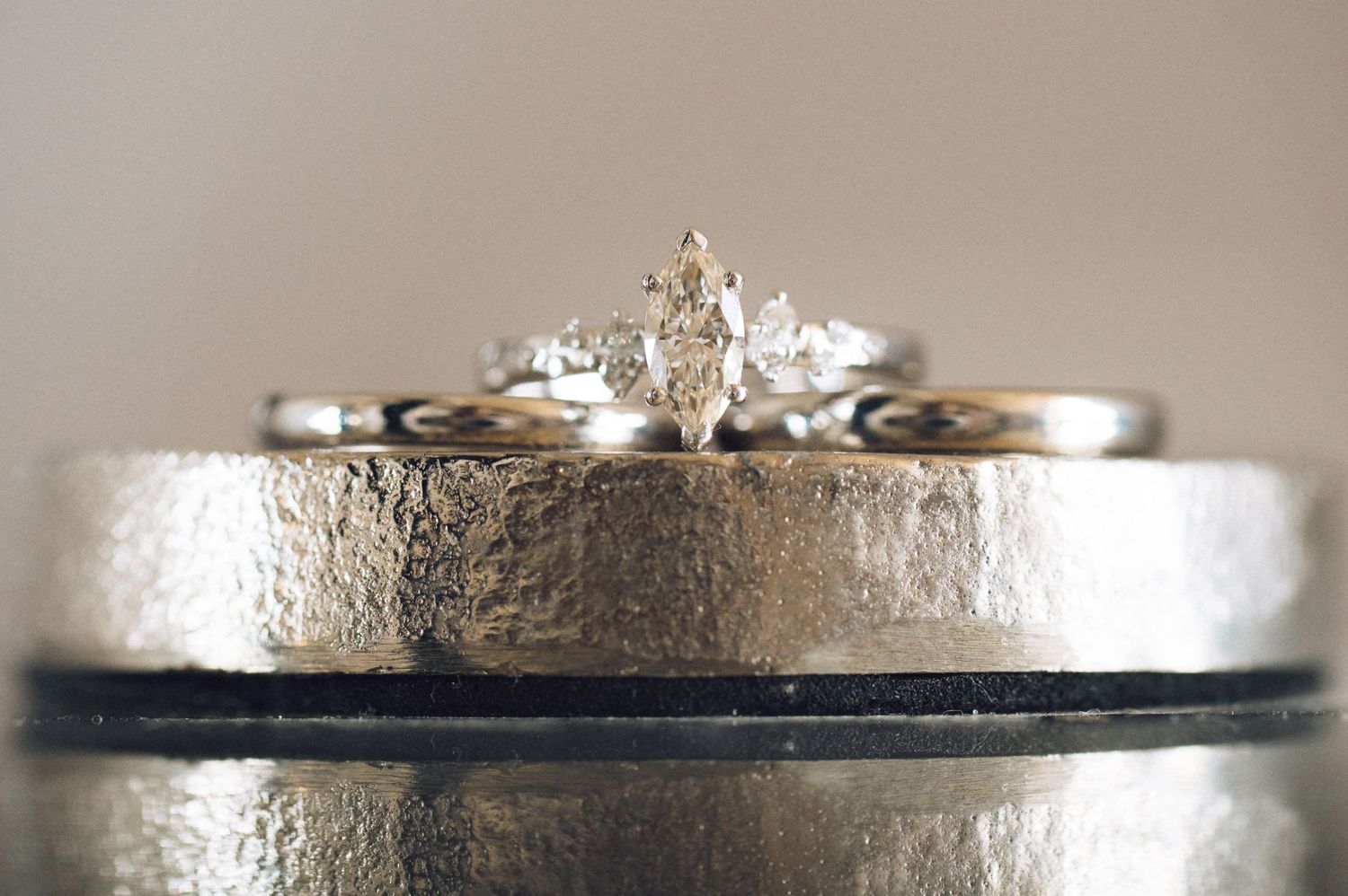 Close-up of a marquise diamond engagement ring resting on textured silver wedding bands.
