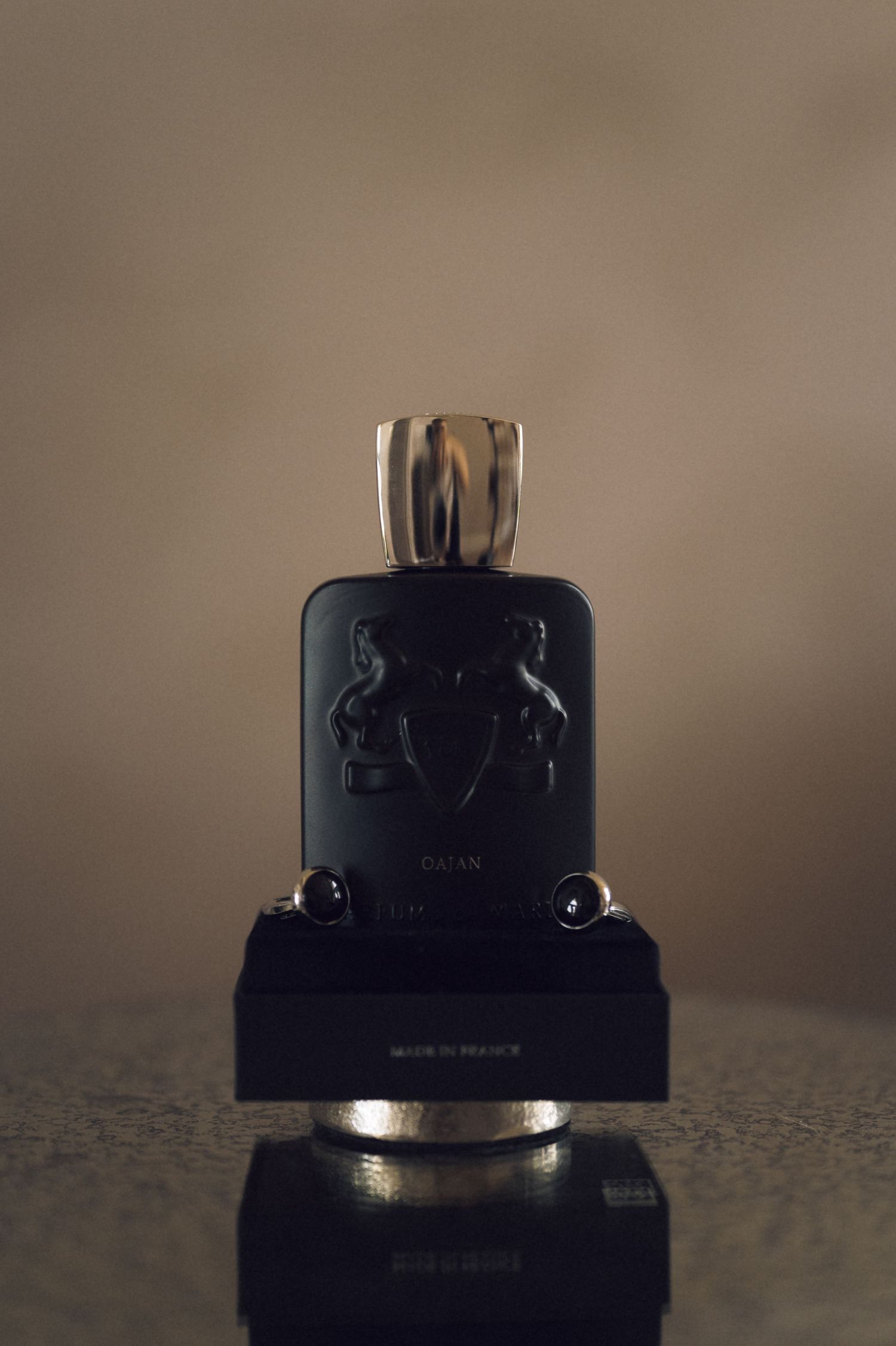 Elegant Parfums de Marly Oajan black perfume bottle with gold cap on reflective surface.